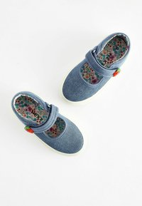 Chaussures en denim bleu avec sangle élastique, bout arrondi et semelle en caoutchouc blanche. Doublure à motif floral et un petit détail d'accent vert et rouge.