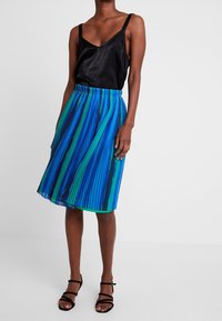 Czarna atłasowa bluzka na ramiączkach zestawiona z plisowaną spódnicą w pionowe niebieskie i zielone paski. Całość uzupełniają czarne sandały na cienkich paskach.