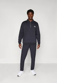 Czarna bluza zapinana na zamek i pasujące dresy, wykonane z miękkiego materiału. Posiadają subtelne akcenty z logo, ściągacze na rękawach i zwężany krój spodni.