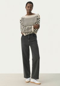 Pull en tricot rayé crème et noir, col large, détails de boutons aux épaules ; associé à un jean noir taille haute et des baskets blanches.