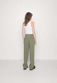 Pantaloni a gamba larga verde oliva con design sartorial, caratterizzati da una parte anteriore piatta e due tasche posteriori, abbinati a un top bianco.
