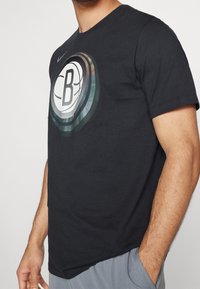 T-shirt en coton noir avec un grand graphique circulaire affichant un logo "B" et des accents de cercles multicolores, col rond et manches courtes.