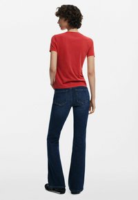 T-shirt rosso a maniche corte abbinato a jeans flare in denim scuro, che mostra un collo semplice e un design classico con tasca. Calzature nere completano il look.