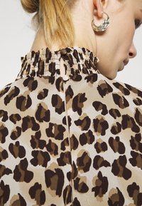 Blůza s leopardím potiskem z měkkého a lehkého materiálu. Obsahuje nařasený dekolt a zapínání na dva knoflíky na zádech pro přiléhavý vzhled.