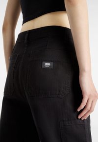 Zwarte denim broek met hoge taille en subtiele stikseldetails, voorzien van twee achterzakken en een Vans logo-label op de rechterzak.