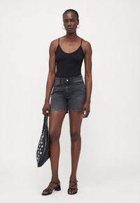 Bodysuit negro sin mangas combinado con pantalones cortos de mezclilla gris oscuro. Llevado con sandalias de tacón negras y un bolso negro con puntos blancos.