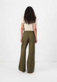 Pantalons larges, de couleur vert olive, en tissu uni, avec une taille haute et des poches avant, associés à une chemise à manches courtes crème.