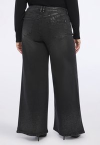 Jeans negros de pierna ancha con una textura ligeramente brillante, costuras visibles y bolsillos traseros. Los dobladillos se ensanchan suavemente, ofreciendo un ajuste relajado.