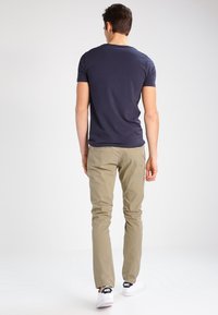 Granatowy bawełniany t-shirt z krótkimi rękawami, w połączeniu z jasnymi khaki spodniami. Obuwie stanowią białe trampki z czarnym logo na pięcie.