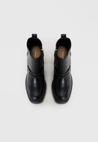 Stivali ankle in pelle nera con suole piatte, cerniere laterali, dettagli elastici e punta tondeggiante. Design semplice con linee pulite e senza decorazioni.