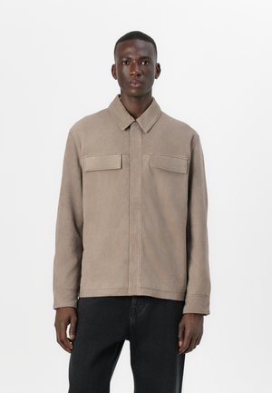 Tan, button-up jacket with a spread collar, two chest pockets, and a straight cut. Made of soft, textured fabric.