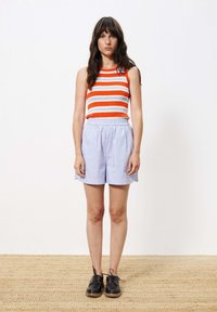 Gestreept mouwloos topje in oranje, blauw en wit; blauw en wit gestreepte shorts; zwarte veterschoenen met een gestructureerde zool.