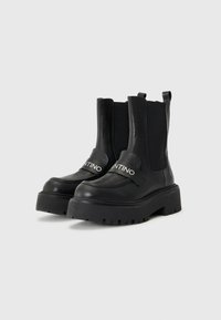 Black leather ankle boots with a chunky rubber sole, elastic side panels, and a branded strap across the front. Smooth texture and sturdy design.