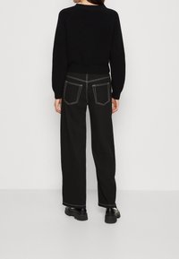 Suéter negro de punto con dobladillo acanalado, combinado con pantalones anchos negros que cuentan con costuras blancas y bolsillos traseros, acompañados de botas negras gruesas.