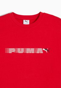 Rød bomulds T-shirt med et hvidt vandret "PUMA" logo og en sort puma grafik på venstre side, med en klassisk rund hals og korte ærmer.