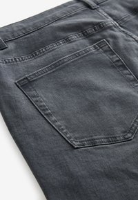 Gros plan sur la poche arrière d'un jean en denim gris foncé montrant les coutures détaillées et la texture du tissu.