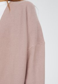 Różowy sweter na drutach z prążkowaną fakturą, dekoltem w kształcie litery V i luźnym krojem. Tkanina delikatnie układa się z subtelnymi detalami ściegu.