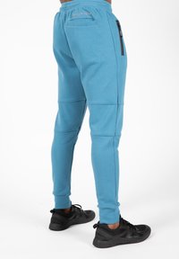 Lichtblauwe sportbroek met een snug fit, voorzien van een ritszak aan de zijkant en een logo op de tailleband. Gecombineerd met zwarte sportschoenen.