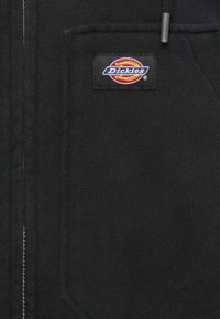 Μαύρο φούτερ με φερμουάρ, κατασκευασμένο από μείγμα βαμβακιού. Διαθέτει έντονη ραφή με το λογότυπο "Dickies", απαλή υφή και πλαινές τσέπες. Ο μηχανισμός του φερμουάρ είναι ορατός.