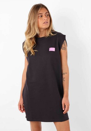 Robe noire surdimensionnée en coton. Présente un patch logo rose sur la poitrine gauche. Manches courtes et coupe décontractée. Texture lisse.