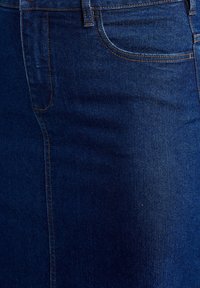 Temno modra denim tkanina z gladko teksturo, ki ima sprednji žep in kontrastni oranžen šiv ob šivih.