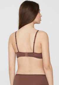 Sujetar marrón con tirantes ajustables y cierre de gancho. Tejido liso y detalles mínimos, con un diseño sencillo.