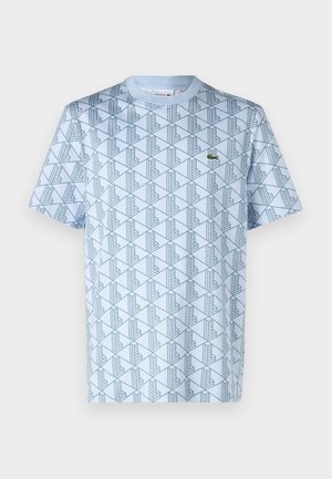T-shirt bleu clair avec un motif géométrique bleu foncé, col rond, manches courtes, et un petit logo vert sur la poitrine gauche.