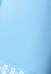 Šviesiai mėlynas medvilninis marškinėlis su raštuota ribine tekstūra ir baltu spausdintu logotipu palei hemą. Turi laisvo stiliaus kirpimą ir standartinę apvalią iškirptę.