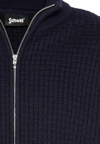 Suéter de punto azul marino con un cuello alto y cremallera plateada en la parte delantera. Presenta un patrón texturizado en toda la tela.