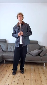 Gray jacket with brown collar, zip front, and side pockets. Paired with black pants and dark shoes. Indoor setting with a couch.