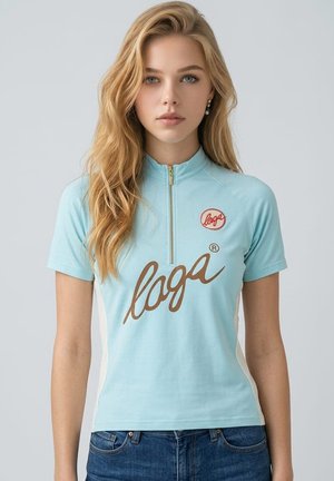 Joven mujer con cabello largo y rubio viste una camiseta azul claro de manga corta con cremallera frontal y un gran logo marrón, combinada con vaqueros azules.