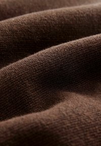 Tissu tricoté marron avec une surface texturée, montrant des fibres douces et en relief ainsi que des plis légers, soulignant sa chaleur et la profondeur de sa couleur.