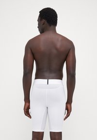 Hvide atletiske shorts med en tætsiddende pasform, der har en tekstureret talje og en baglomme med lynlås. Glat stof, længde til midten af låret.