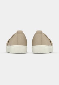 Beige canvas sneakers with a textured design, featuring a white rubber sole and loops at the heel for easy wear.