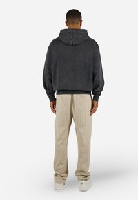 Dark grey hooded sweatshirt with a relaxed fit and ribbed cuffs, paired with beige corduroy pants. Sneakers complete the outfit.