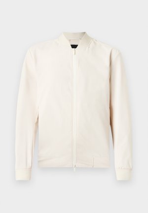 Jasno beżowa kurtka bomberka z zapięciem na zamek, prążkowanym kołnierzem i mankietami, wykonana z gładkiego, lekkiego materiału. Posiada boczne kieszenie i minimalistyczny design.