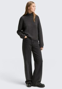 Dunkelgrauer Rollkragenpullover mit gerippter Stricktextur, kombiniert mit weit geschnittenen schwarzen Hosen und schwarzen Plateauschuhen.