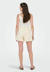 Shorts ligeros color beige con bordados florales verdes, con un corte relajado y una cintura elástica, combinados con una camiseta sin mangas blanca.