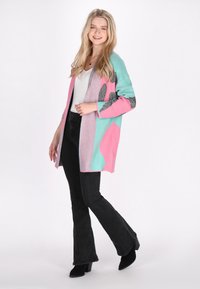 Cardigan lavorato a maglia con colori rosa, turchese e grigio, dotato di maniche lunghe, apertura anteriore e un fit largo. Abbinato a jeans neri svasati.