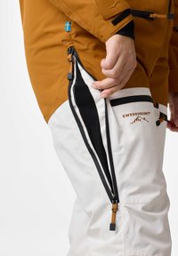 Ski jacket in brown with a Swedish flag detail, featuring zippers on white pants with black accents and "SWEDEMOUNT" logo. Smooth texture.