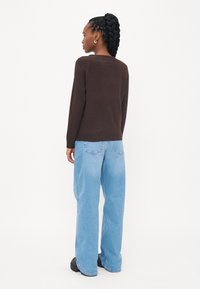Brun strikket genser kombinert med lyseblå vide jeans, med en avslappet passform og ribbede mansjetter. Svart kraftige sko fullfører antrekket.