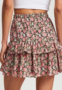 Jupe à volants florale avec une base noire ornée de motifs de fleurs roses et vertes, taille élastique et ourlet à volants superposés.