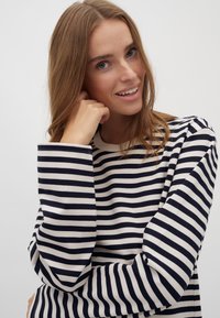 Randig långärmad topp i marinblått och krämvitt, med horisontella ränder, rund hals och mjukt tyg. Ärmarna är något oversized.