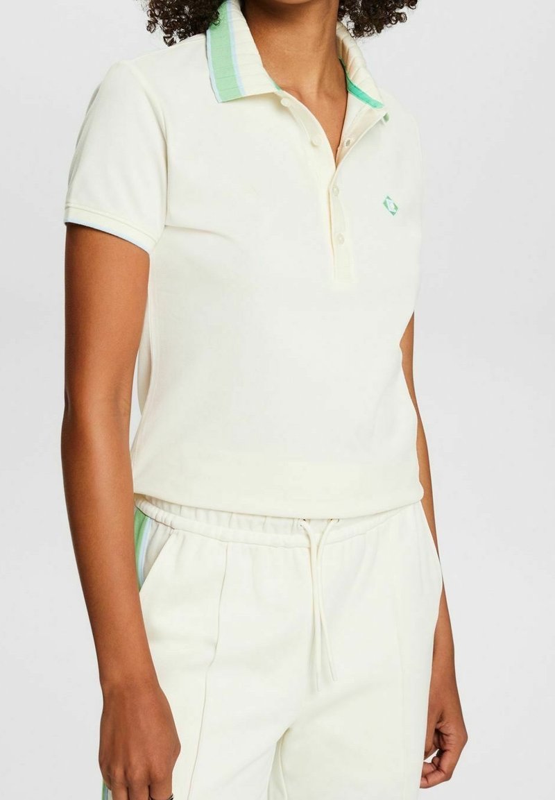 Polo crème avec un col rayé vert menthe, doté d'une patte de boutonnage à trois boutons et d'un logo sur la poitrine. Tissu doux, coupe ajustée.