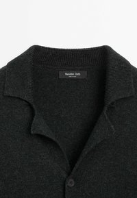 Cardigan noir en maille avec col plié et un bouton visible, montrant l'étiquette « Massimo Dutti » cousue à l'intérieur de l'encolure.