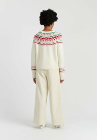 Cream sweater with multicolored geometric patterns at the yoke. Paired with light-colored, wide-leg pants, featuring a soft texture.
