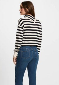 Maglione a righe in nero e crema, con scollatura a V e polsini a coste, abbinato a jeans in denim blu con vestibilità slim e dettagli minimi.