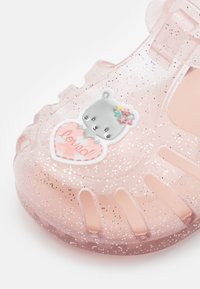 Sandalia de gel translúcida rosa con purpurina, con un aplique en forma de oso que sostiene una etiqueta en forma de corazón que dice "amado" y acentos florales.