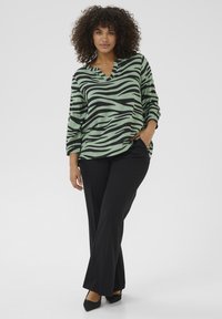 Blusa a righe verde e nera con scollo a V e maniche a tre quarti, abbinata a pantaloni neri svasati e scarpe con tacco nere.