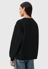 Felpa nera oversize in materiale morbido, con colletto rotondo e maniche lunghe, abbinata a jeans baggy azzurri.